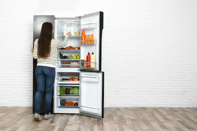 Young woman taking yoghurt out of refrigerator indoors, space for text