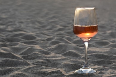 Photo of Glass of tasty rose wine on sandy beach, space for text
