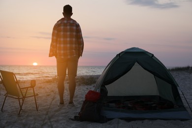 Man enjoying sunset near camping tent on beach, back view