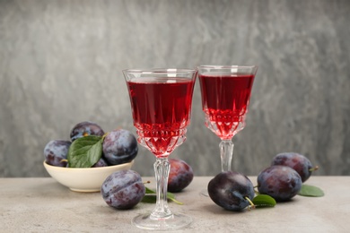 Delicious plum liquor and ripe fruits on table against grey background. Homemade strong alcoholic beverage