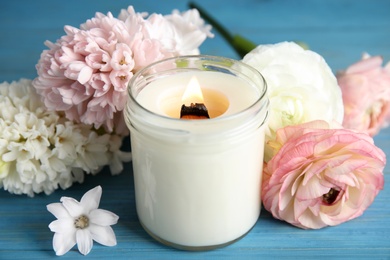 Scented candle with burning wooden wick and flowers on blue table, closeup