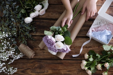 Florist making beautiful wedding bouquet at wooden table, top view