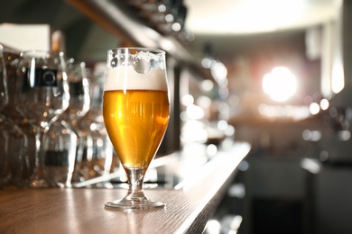 Photo of Glass of beer on wooden counter in pub. Space for text