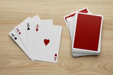 Four aces and deck of playing cards on wooden table, flat lay