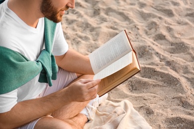 Young man reading book on sandy beach, closeup