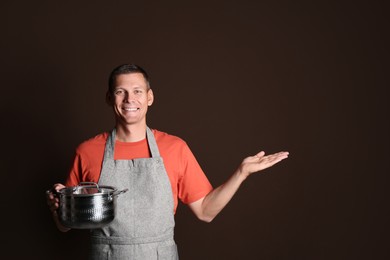 Photo of Happy man with cooking pot on brown background. Space for text