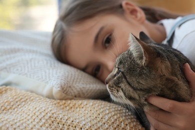 Photo of Cute little girl with her cat on bed at home, closeup. Childhood pet
