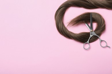 Professional hairdresser scissors and hair strand on pink background, flat lay with space for text. Haircut tool