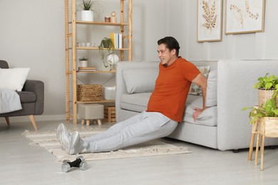 Overweight man doing exercise near sofa at home