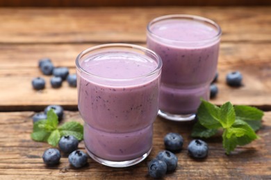 Glasses of blueberry smoothie with mint and fresh berries on wooden table