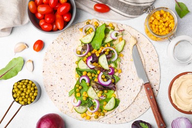 Photo of Tortilla with hummus and vegetables on light table, flat lay