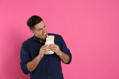 Man eating delicious shawarma on pink background, space for text