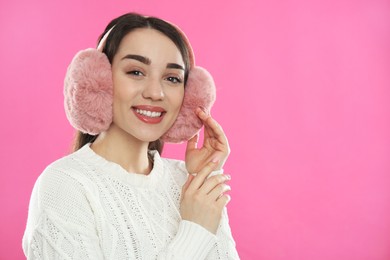 Beautiful young woman wearing earmuffs on pink background. Space for text