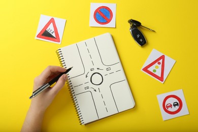 Woman with workbook for driving lessons and road signs on yellow background, top view. Passing license exam