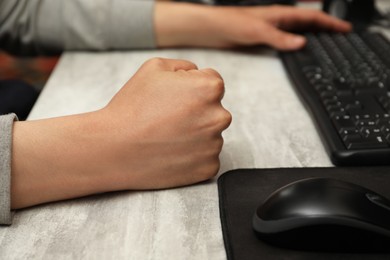 Photo of Angry man with clenched fist working on computer at table, closeup