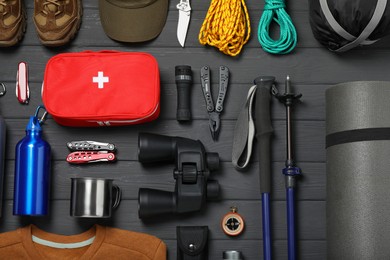 Flat lay composition with trekking poles and other hiking equipment on dark grey wooden background