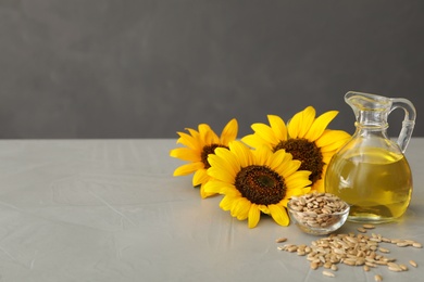 Sunflowers, jug of oil and seeds on grey table, space for text