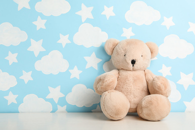 Teddy bear on white table near wall with painted blue sky, space for text. Baby room interior