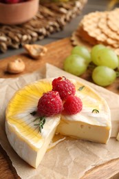 Brie cheese served with berries and honey on wooden board, closeup