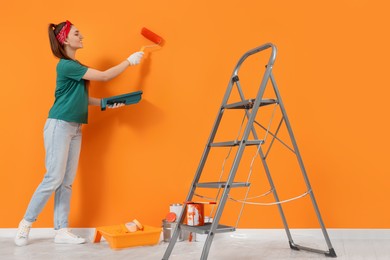 Photo of Designer painting orange wall with roller indoors