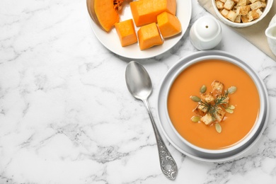 Tasty creamy pumpkin soup with croutons, seeds and dill in bowl on white marble table, flat lay. Space for text