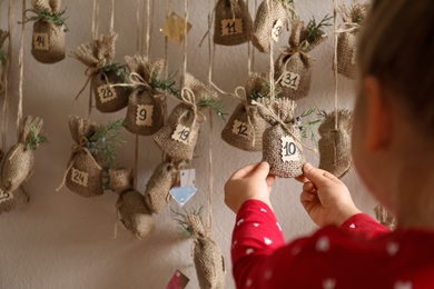 Photo of Little girl taking gift from New Year advent calendar indoors, closeup
