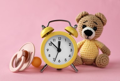 Alarm clock, baby dummy and toy bear on pink background. Time to give birth