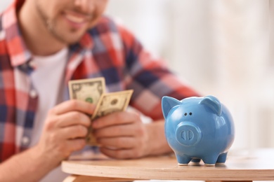 Man with piggy bank and money at home, closeup