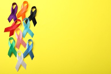 Photo of Colorful ribbons on yellow background, flat lay with space for text. World Cancer Day