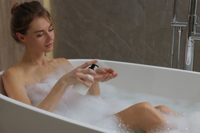 Beautiful woman pouring shower gel onto hand in bath indoors