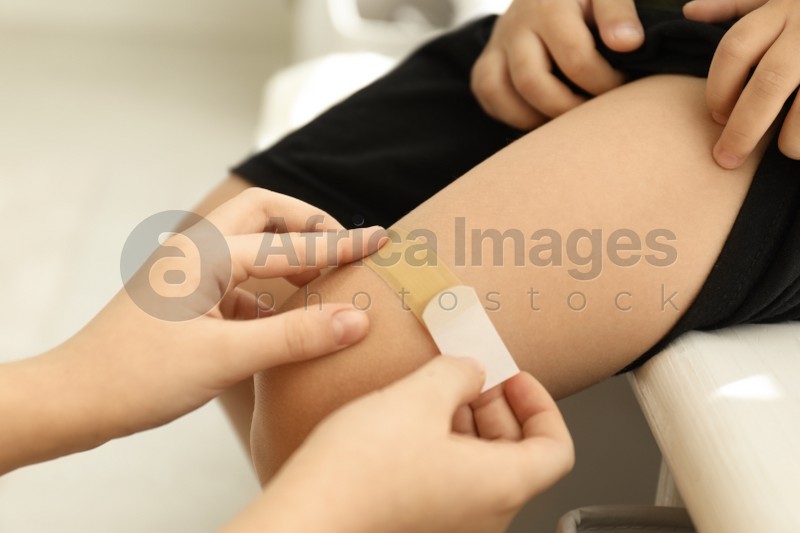 Photo of Sister putting sticking plaster onto little brother's leg indoors, closeup