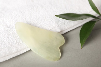 Photo of Jade gua sha tool, green leaf and towel on grey table, closeup