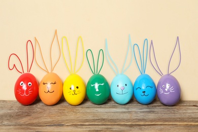 Colorful eggs as Easter bunnies on wooden table against beige background