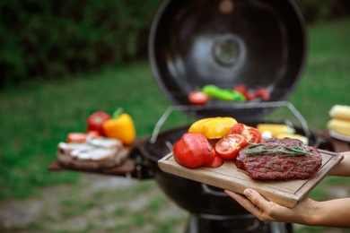 Woman holding wooden board with grilled vegetables and steak outdoors, closeup. Summer barbecue