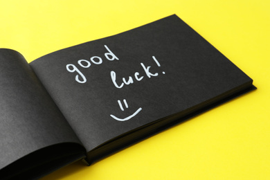 Notebook with phrase GOOD LUCK and funny face on yellow background, closeup