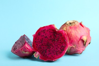 Photo of Delicious cut and whole red pitahaya fruits on light blue background