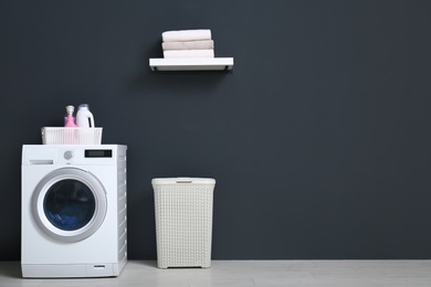 Photo of Modern washing machine, laundry basket and shelf with towels in bathroom. Space for text