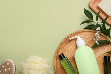 Flat lay composition with shower gel bottles on light green background, space for text