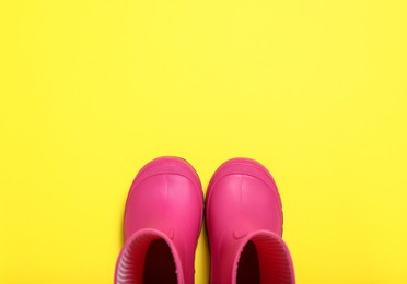 Pair of bright pink rubber boots on yellow background, top view. Space for text