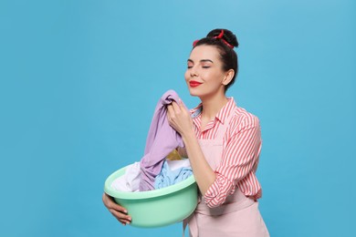 Housewife holding basin with clothes on light blue background