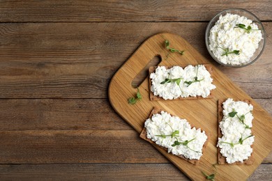 Photo of Crispy crackers with cottage cheese and microgreens on wooden table, flat lay. Space for text
