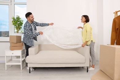 Photo of Happy couple taking plastic film from sofa in new apartment. Moving day