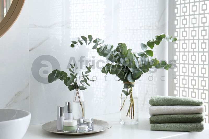 Fresh eucalyptus branches and cosmetic products on countertop in bathroom