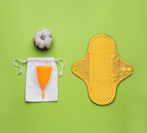 Reusable cloth pad, menstrual cup and cotton flower on green background, flat lay