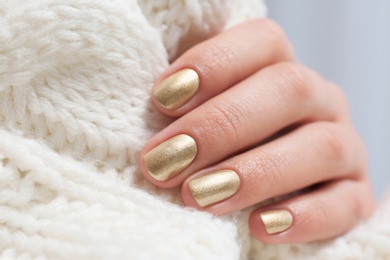 Woman with golden manicure holding knitted fabric, closeup. Nail polish trends