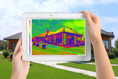 Woman detecting heat loss in house using thermal viewer on tablet, outdoors. Energy efficiency