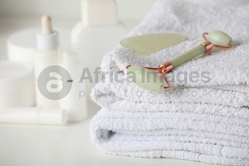 Natural face roller, gua sha tool and towels on white table, closeup