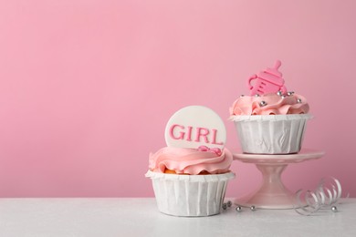 Photo of Baby shower cupcakes with toppers on white table against pink background, space for text