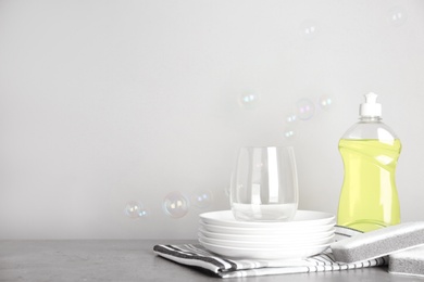 Cleaning product, plates and soap bubbles on grey background, space for text. Dish washing supplies
