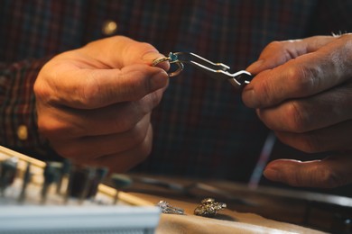 Photo of Professional jeweler working with ring at wooden table, closeup